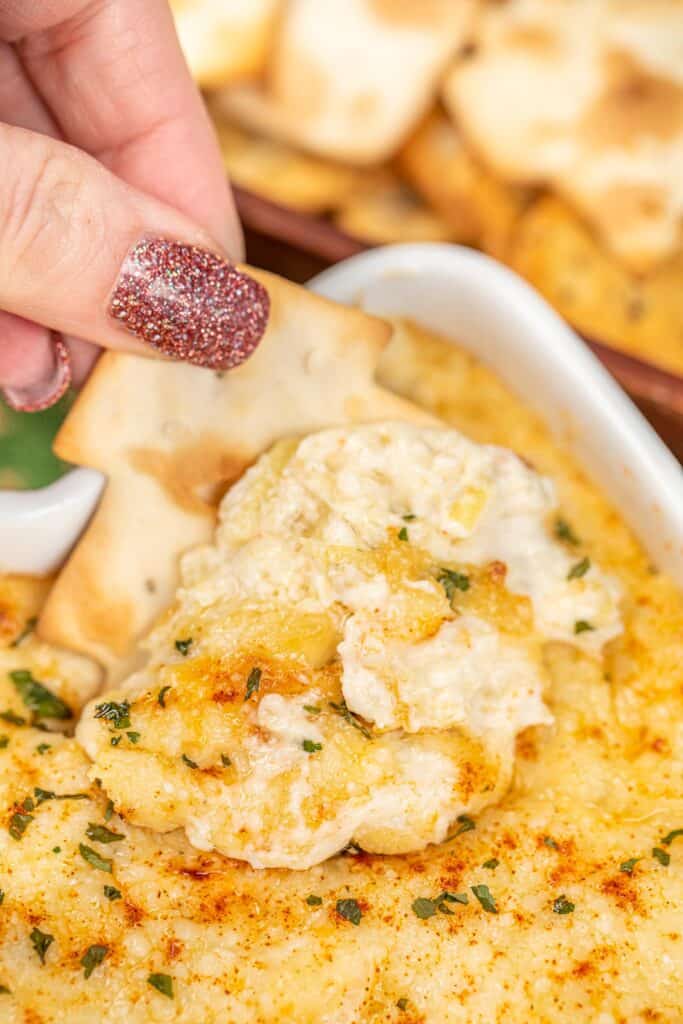 scooping artichoke dip with a chip from a baking dish
