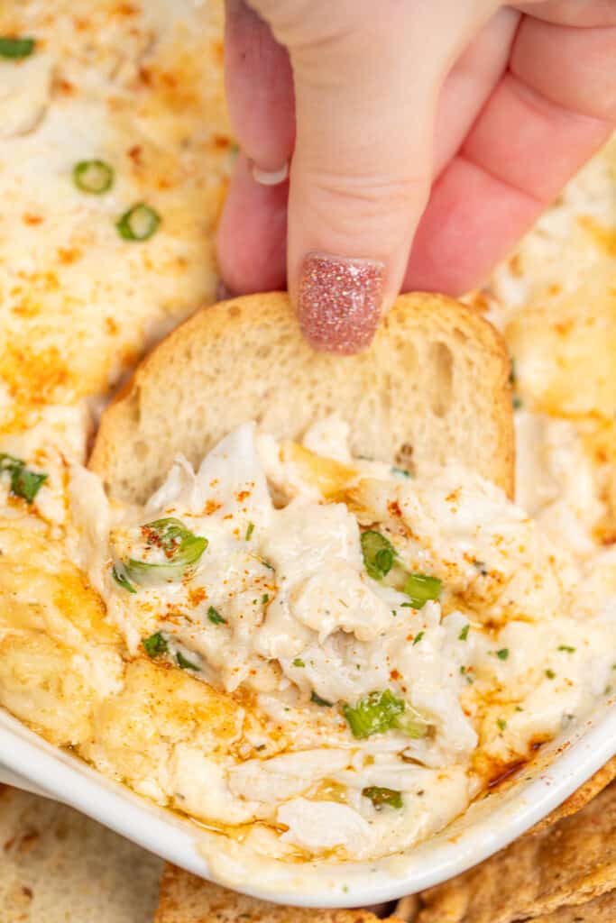 dipping toast into a baking dish of crab dip
