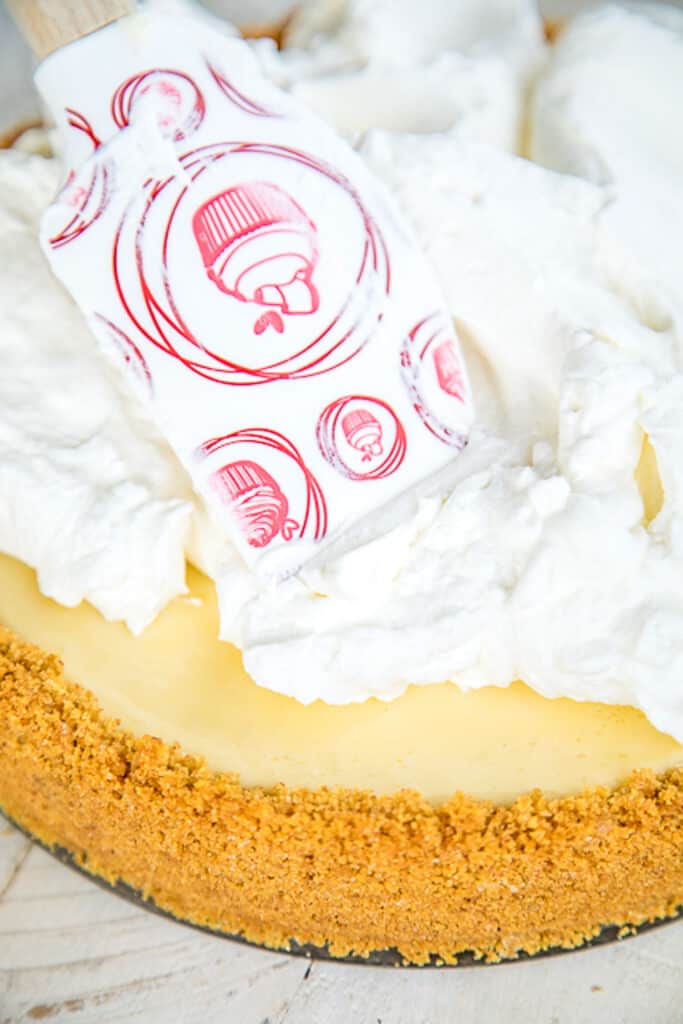 spreading whipped cream on top of a lemon pie
