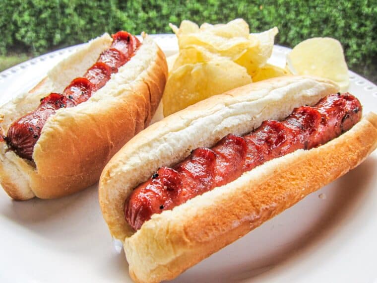 grilled hot dogs in buns on a plate with chips