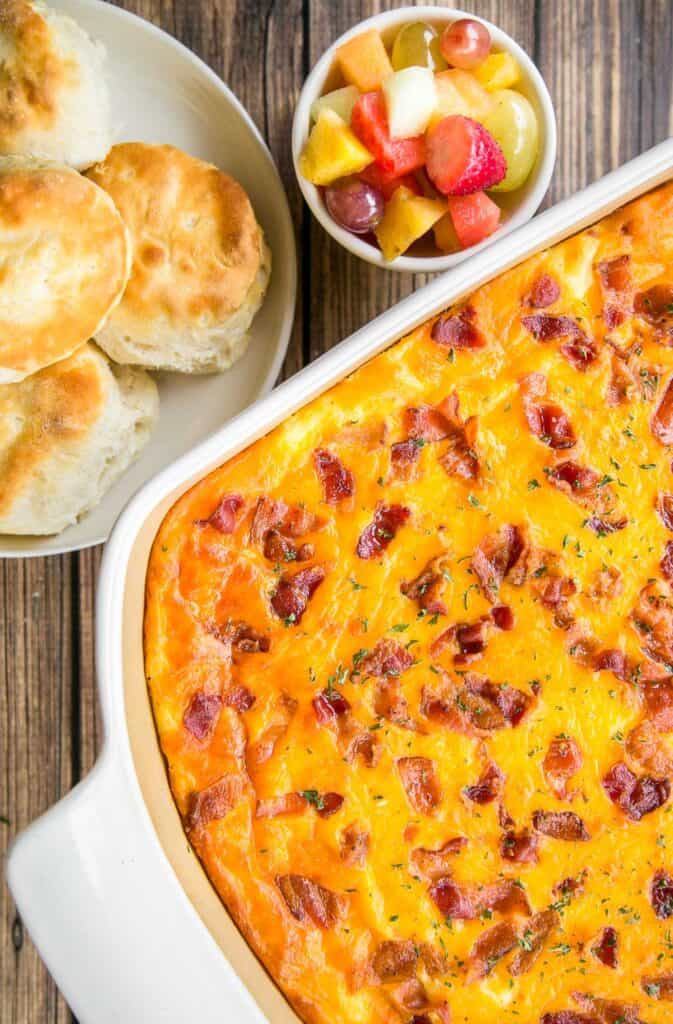 baking dish of bacon and cheese grits with biscuits and fruit