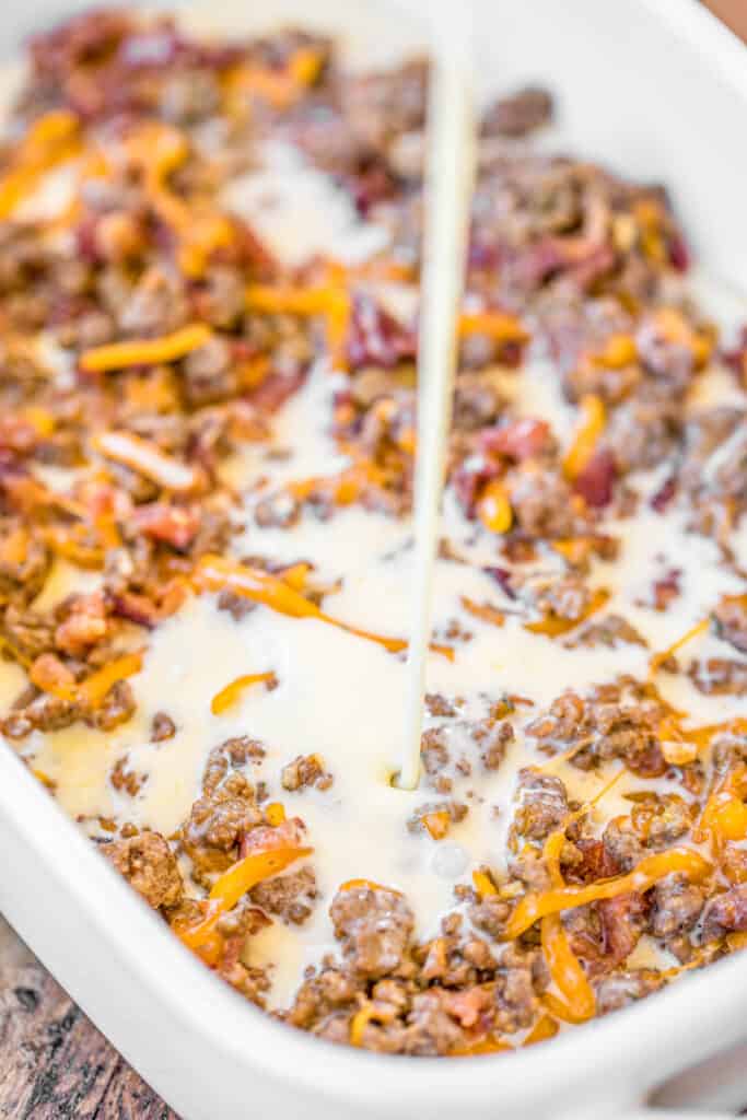 pouring egg mixture over ground beef bacon and cheese in a baking dish