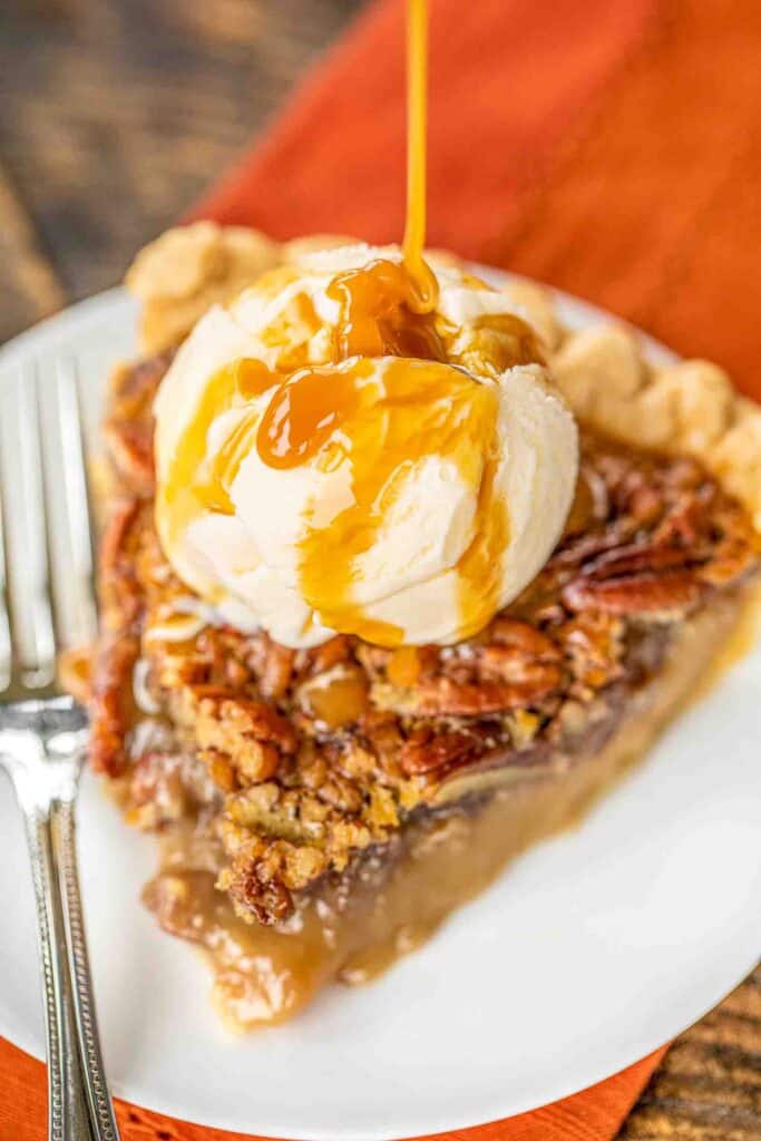 pouring caramel over ice cream on top of a slice of pecan pie