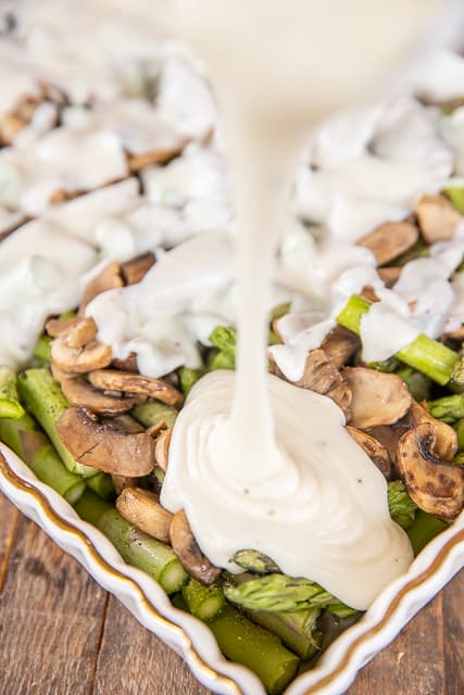 pouring cheese sauce over asparagus and mushrooms