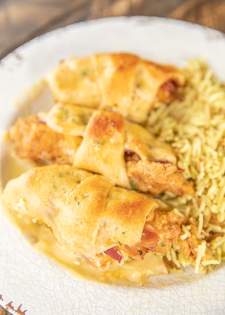 Crack Chicken Roll Ups - our favorite weeknight meal!! Frozen chicken fingers, cheddar cheese, bacon and ranch wrapped in crescent rolls and topped with cream of chicken soup and milk. Seriously delicious!! I always have to double the recipe for my family. We never have any leftovers! #chicken #casserole #chickencasserole #weeknightdinner #easychickenrecipe