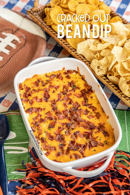 Cracked Out Bean Dip - SO addictive! Bean dip loaded with cheddar bacon and ranch. I could NOT stop eating this yummy dip. The flavors are amazing! Refried beans, taco seasoning, sour cream, ranch, bacon and cheddar cheese. Can make ahead of time and refrigerate until ready to bake. Serve with fritos and tortilla chips. This dip is always the first thing to go at our tailgates! I never have any leftovers! YUM! #dip #beandip #tailgating #appetizer #partyfood