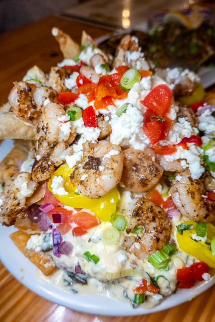 Greek Shrimp Nachos from FloraBama Yacht Club -  Fried wonton chips smothered in a spinach-feta-cream sauce topped with grilled Gulf shrimp, tomatoes, crumbled feta, Kalamata olives, peppadews, banana peppers, green onion, and red onion