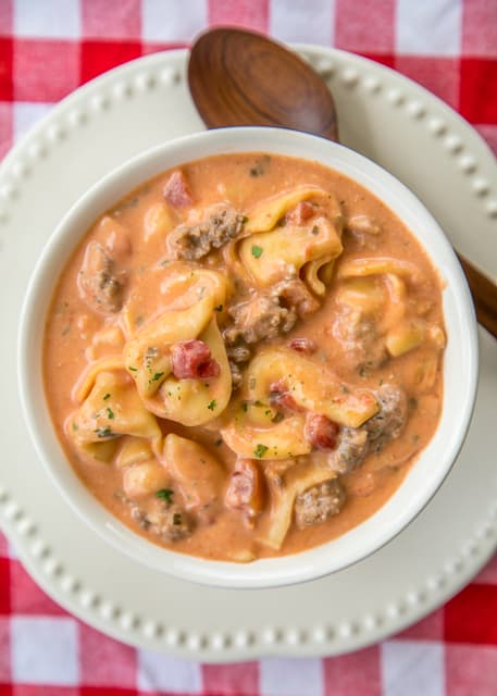 Slow Cooker Tomato Tortellini Soup - seriously delicious! Everyone LOVED this no-fuss soup recipe. Just dump everything in the slow cooker and let it work its magic. Serve soup with some crusty bread for an easy weeknight meal the  whole family will enjoy! Chicken broth, tomato soup, diced tomatoes, Italian sausage, chive and onion cream cheese and cheese tortellini combine to make THE BEST tomato soup EVER!