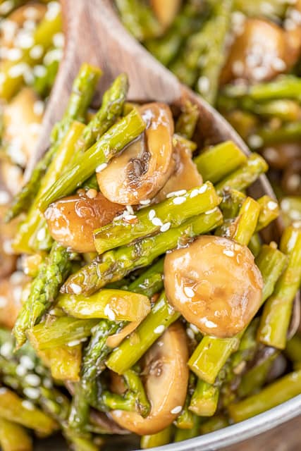 scooping asparagus and mushrooms out of a skillet