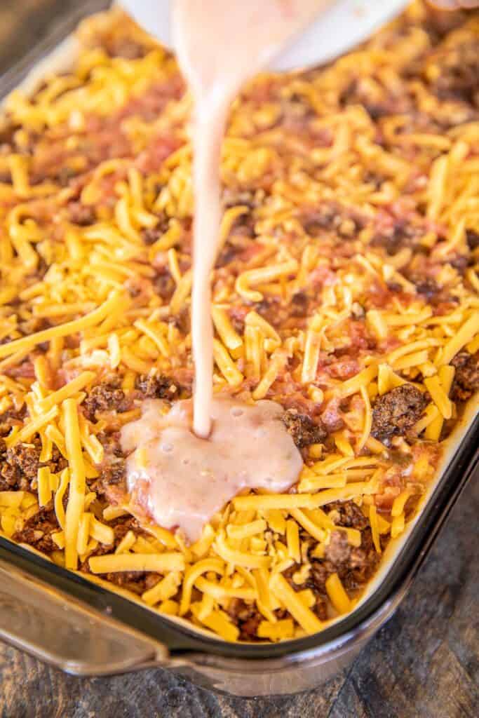 pouring liquid over taco casserole in baking dish
