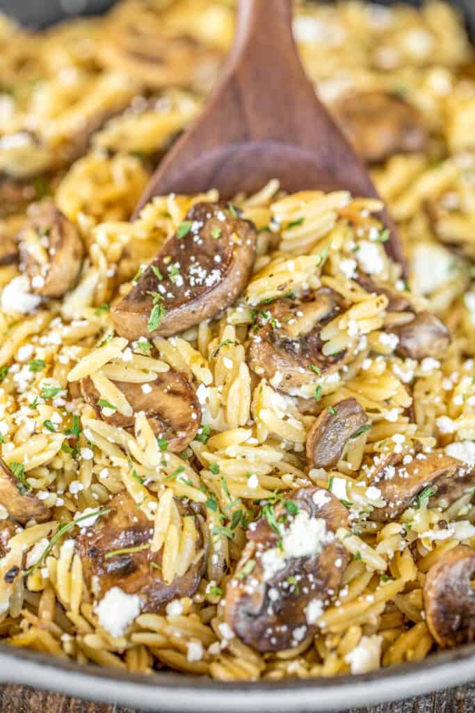 spooning orzo pasta with feta and mushrooms from the skillet