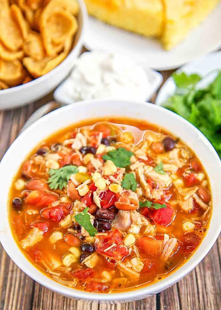 Chicken Taco Soup Recipe - Chicken, beans, corn, tomatoes, Ranch mix and taco seasoning. Can be made two different ways. On the stovetop with some rotisserie chicken or in the slow cooker with some boneless chicken breasts. Either way, it is super delicious and packed FULL of flavor! Serve with some cornbread for a delicious meal!