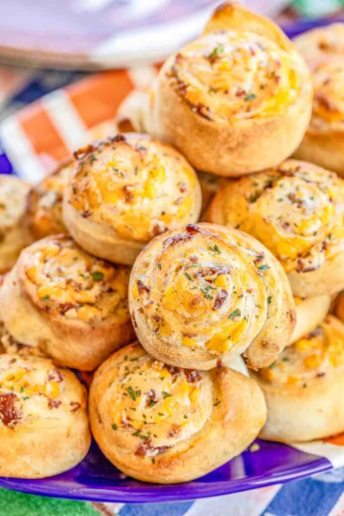 Crack Pinwheels - SO addictive!!! Ranch seasoning, cream cheese, cheddar cheese, and bacon baked in pizza dough - I could eat the whole batch! Great as an appetizer or with soup or stew. Tastes great hot out of the oven or at room temperature. These cheesy bread pinwheels don't last long! #cheddar #bacon #ranch #tailgating #tailgatingrecipes #bread #appetizer