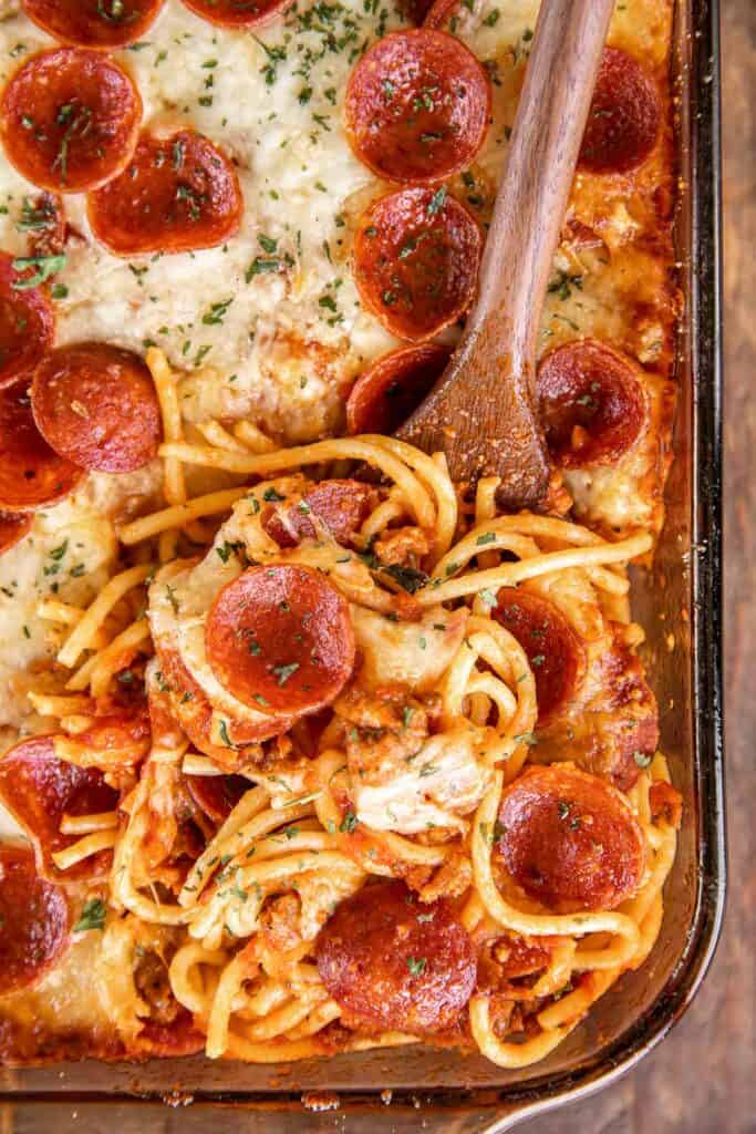 scooping pepperoni spaghetti casserole from baking dish