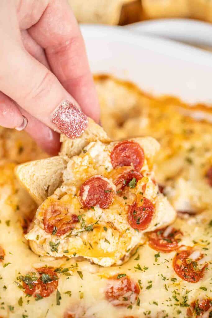 serving pepperoni pizza dip on bread from baking dish