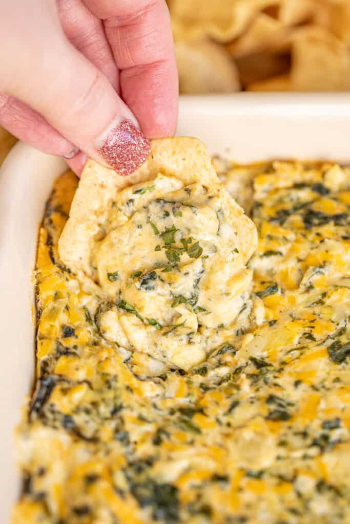 scooping spinach dip from baking dish with a chip