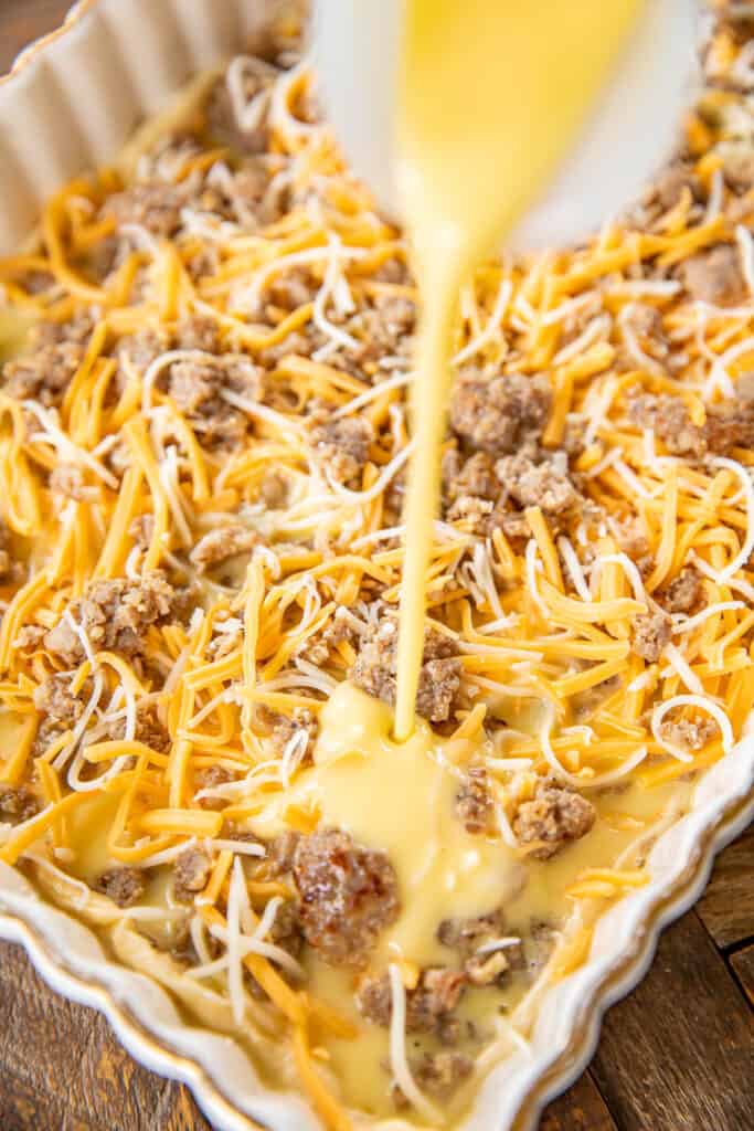 pouring egg custard over sausage and cheese in baking dish