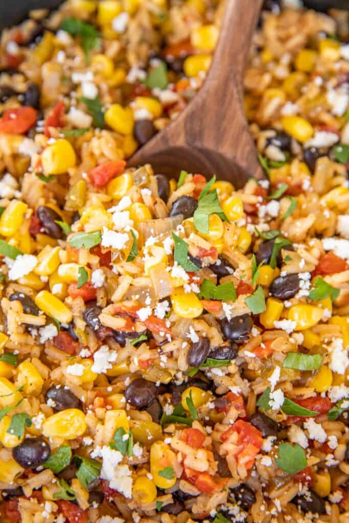spooning rice with black beans, peppers and corn from skillet