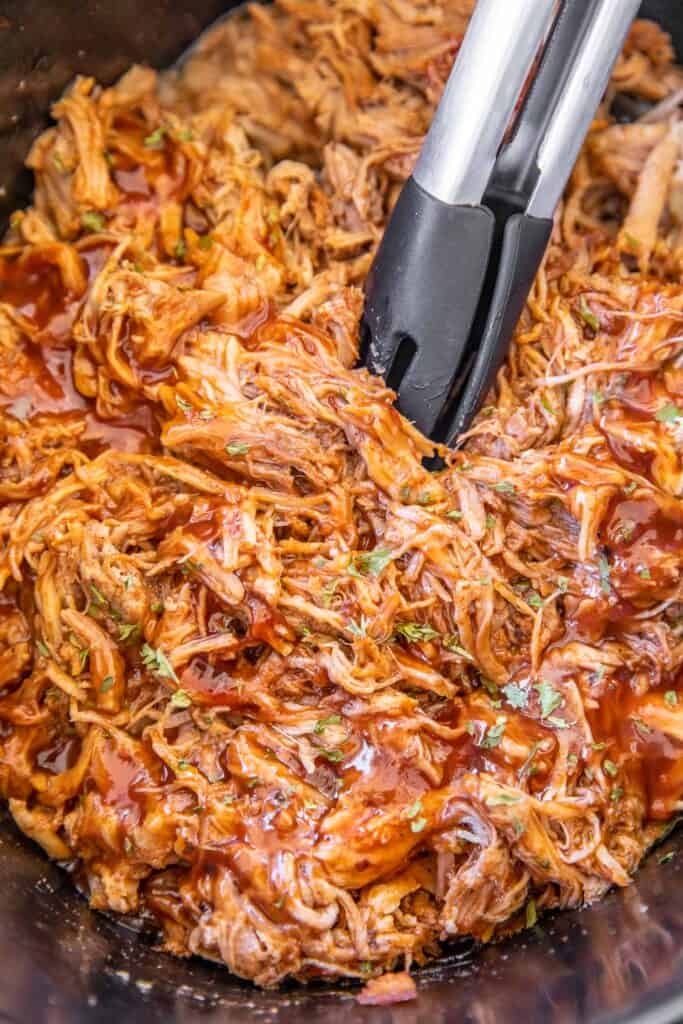 slow cooker of pulled pork with tongs in it