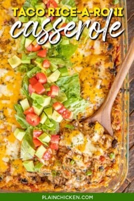 casserole dish of taco casserole with a spoon in it and topped with lettuce tomatoes and avocado