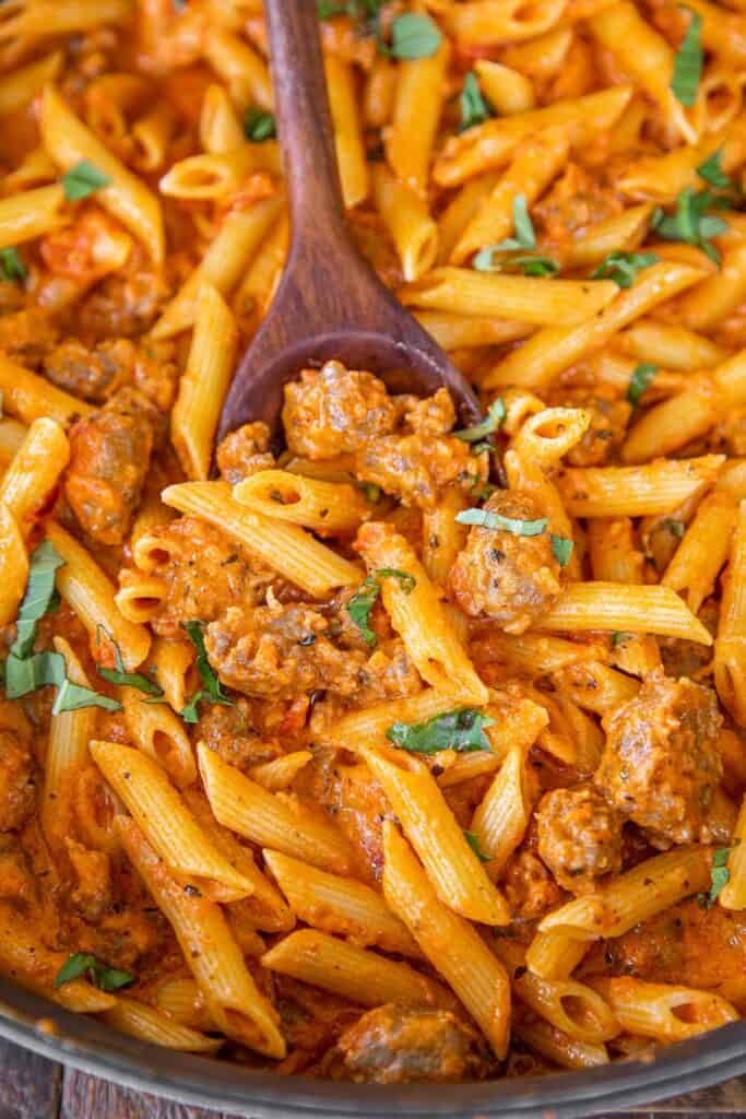 spooning penne pasta with sausage from skillet