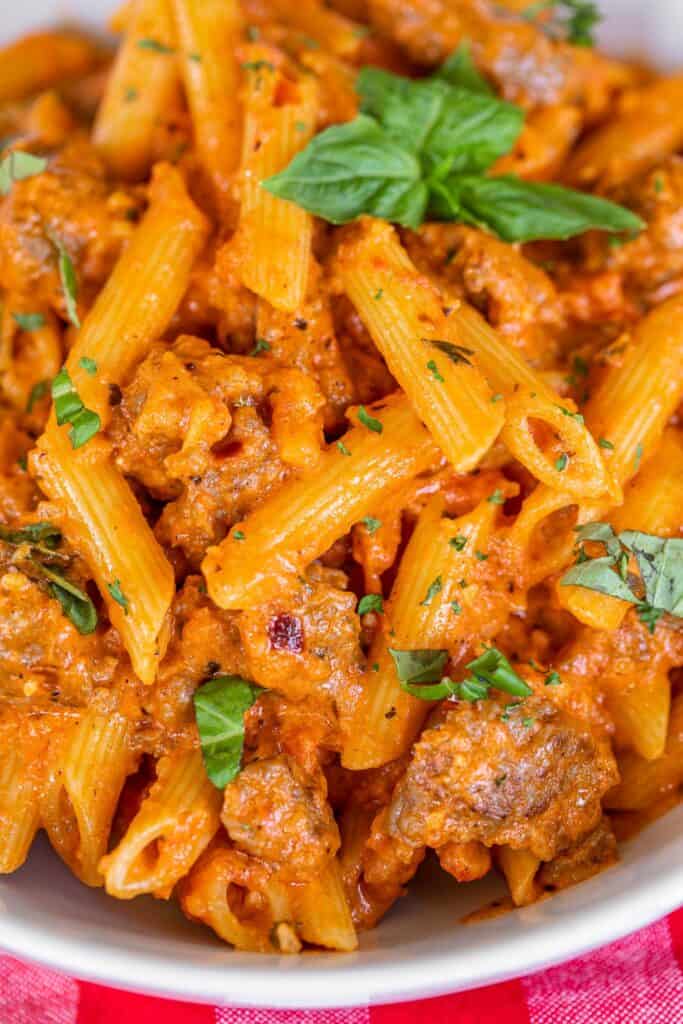 close up of penne pasta with sausage and basil