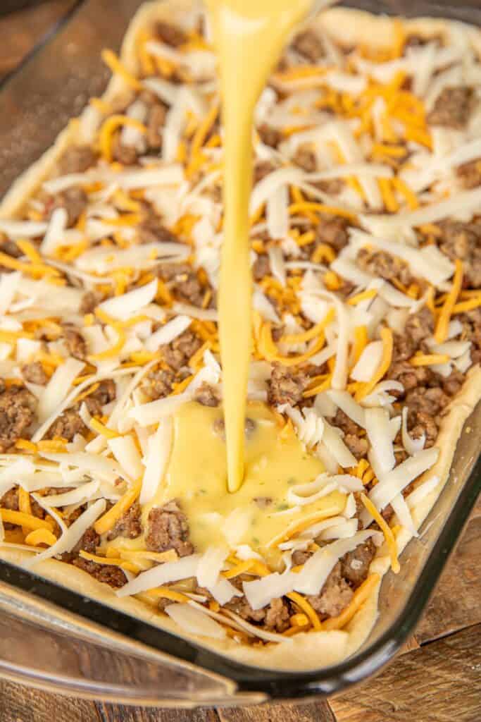 pouring milk and eggs over sausage and cheese in baking dish