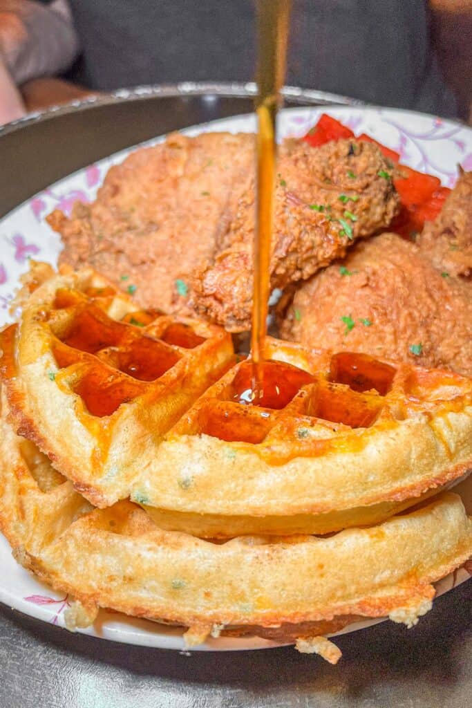 pouring syrup over chicken and waffles
