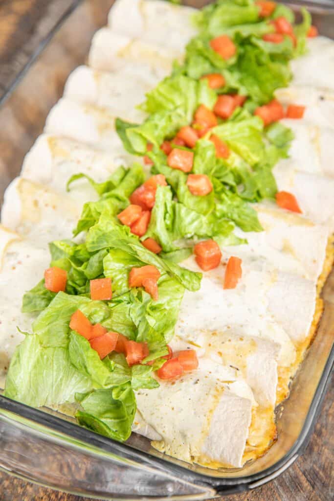 baking dish of chicken enchiladas topped with lettuce and tomato