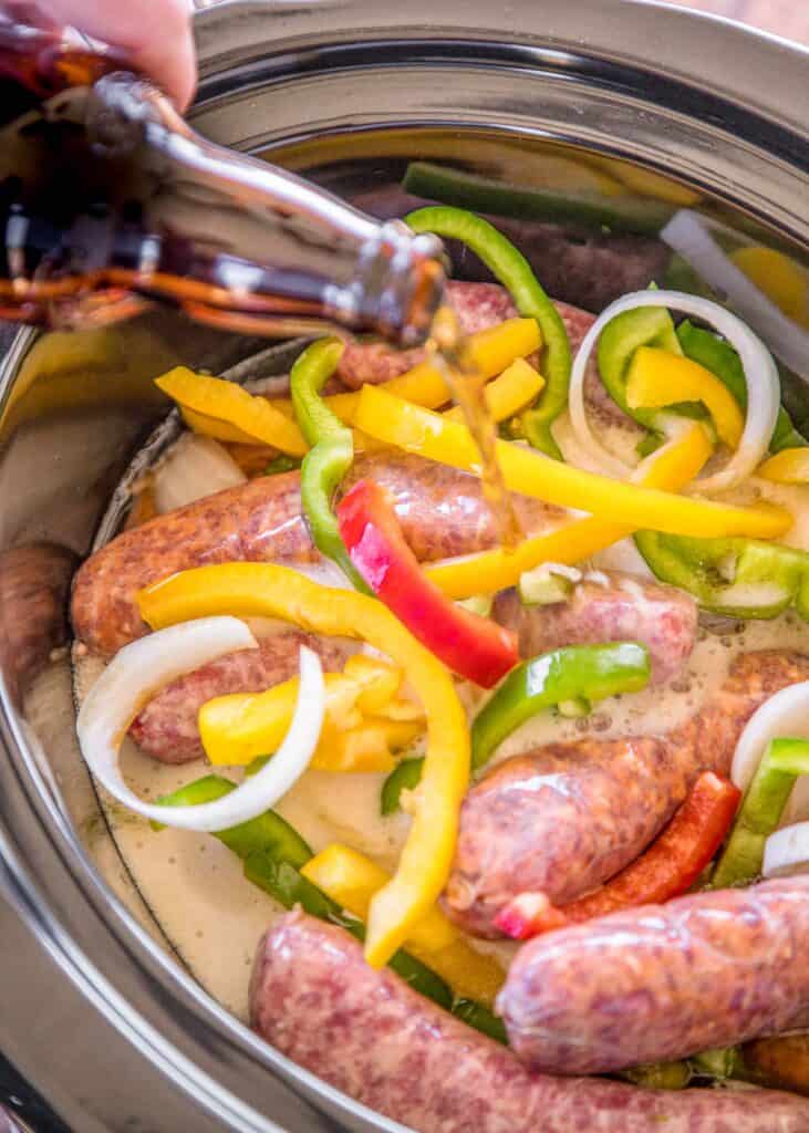 pouring beer over sausages and peppers in the slow cooker