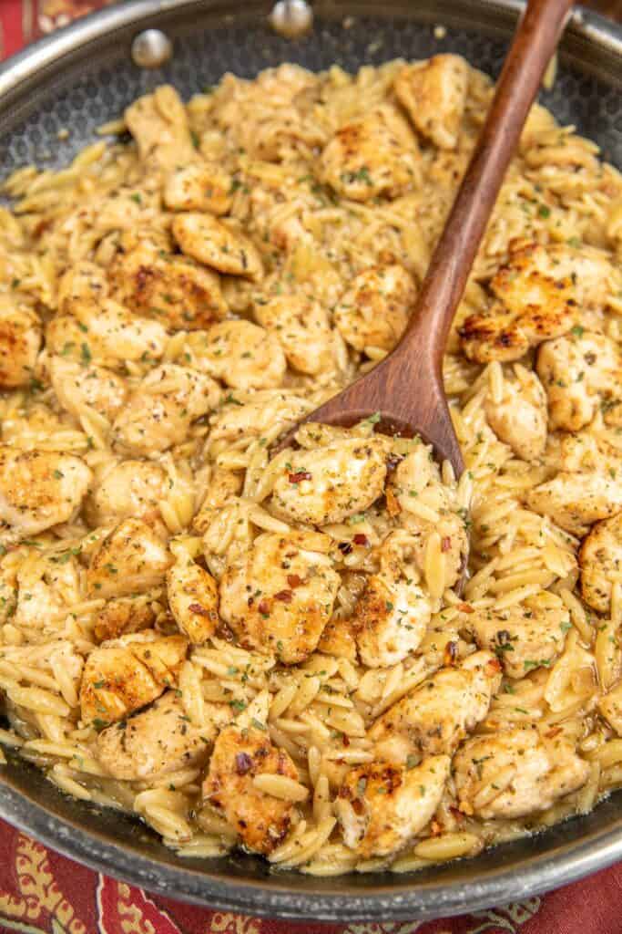 scooping chicken and orzo from skillet