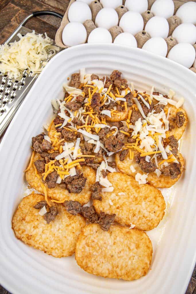 sausage and cheese on top of hash brown patties in a baking dish