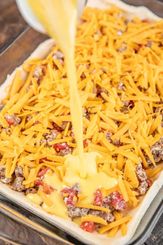 pouring egg mixture over sausage and cheese in baking dish