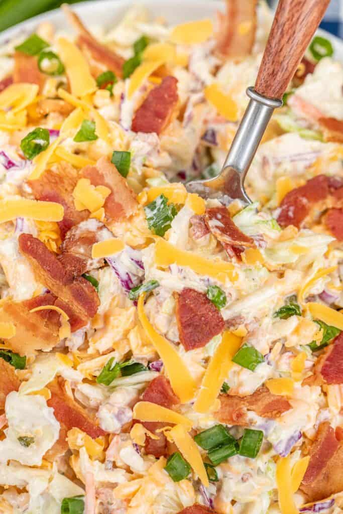 sticking a fork into a bowl of slaw with cheese and bacon