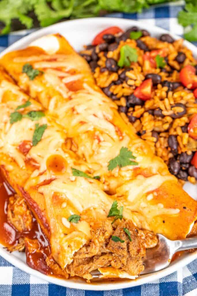 cutting into a plate of bbq pork enchiladas with a fork
