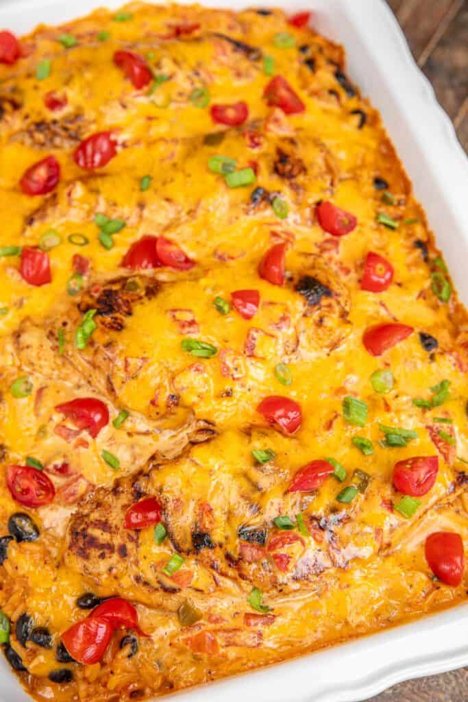 baking dish of queso smothered chicken topped with tomatoes