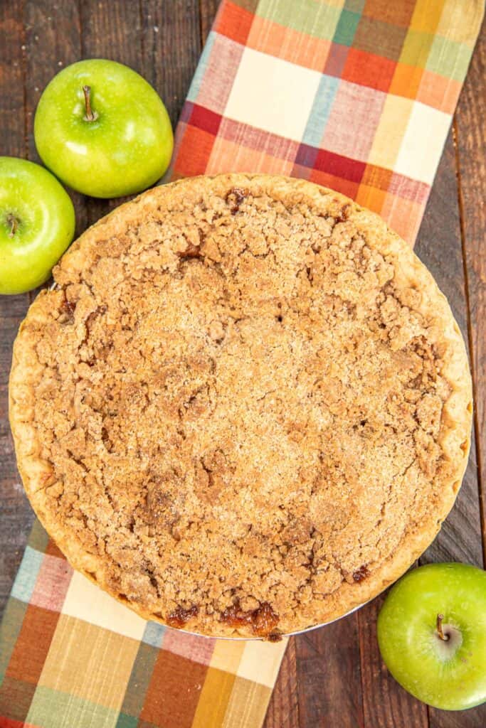 whole apple pie on a table with 3 apples on the side