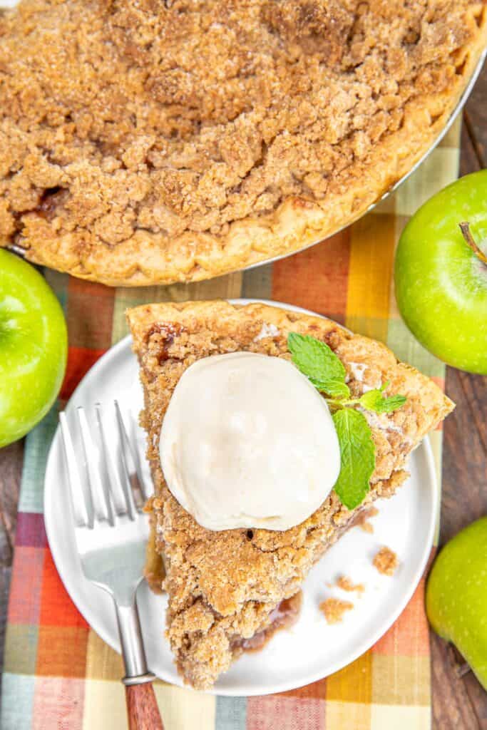 slice of apple pie topped with ice cream and mint on a plate with a whole pie in the background