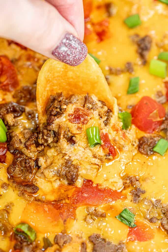 scooping beef enchilada dip from a baking dish with a Frito chip