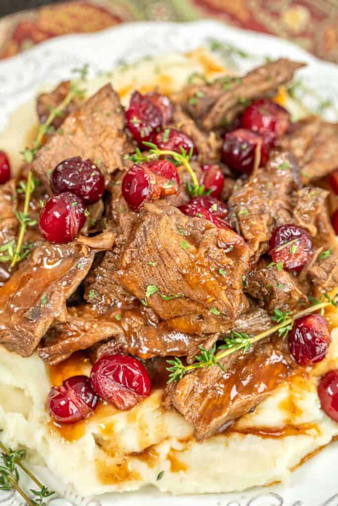 plate of cranberry pot roast over mashed potatoes on a table