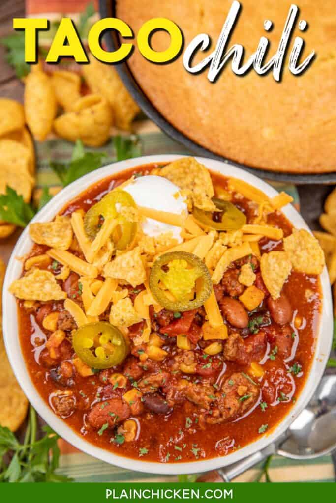 bowl of chili topped with sour cream, cheese, jalapenos, and crusted fritos in front of a pan of cornbread with text overlay