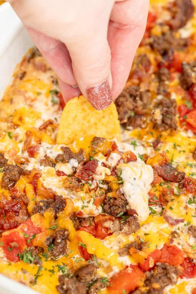 scooping bacon cheeseburger dip from a baking dish with a Frito corn chip