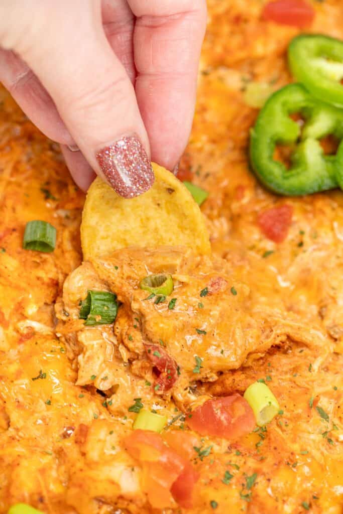 scooping mexican chicken dip from a baking dish with a Frito corn chip