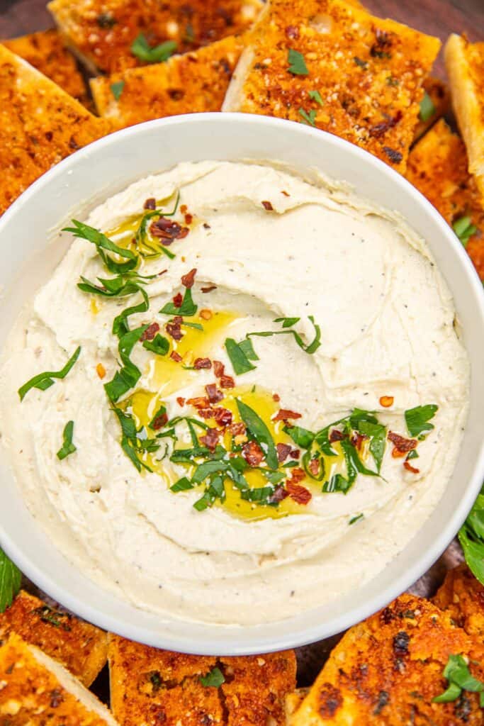 bowl of feta dip topped with basil, red pepper flakes and olive oil on a platter with bread slices