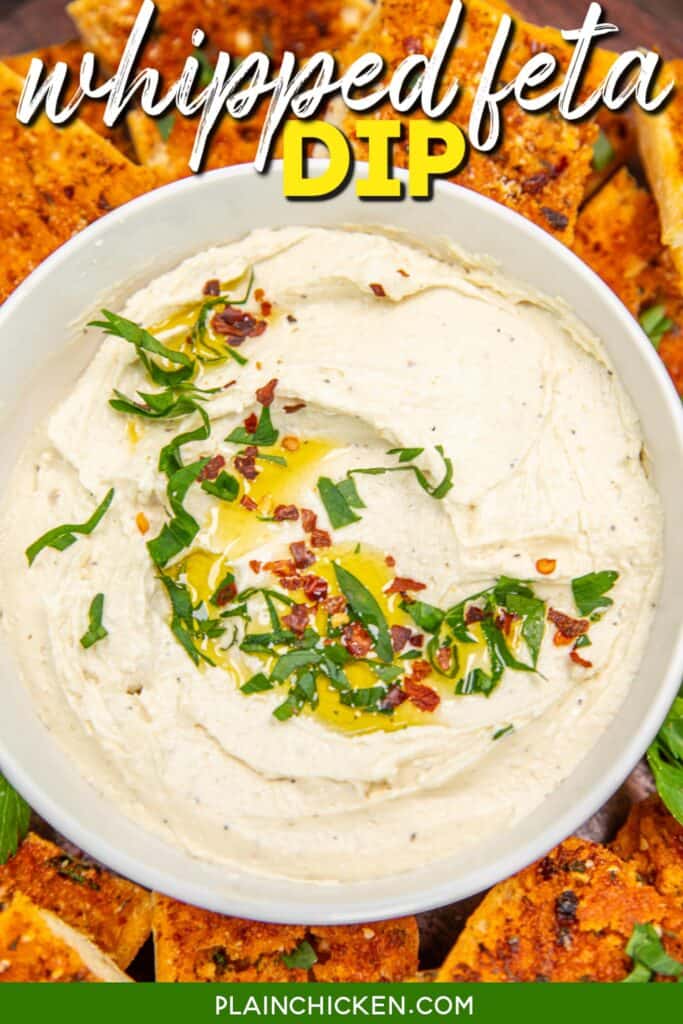 bowl of feta dip topped with basil, red pepper flakes and olive oil on a platter with bread slices with text overlay