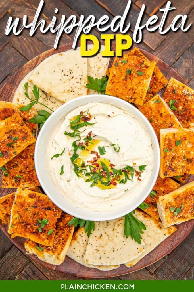 bowl of feta dip topped with basil, red pepper flakes and olive oil on a platter with bread slices with text overlay