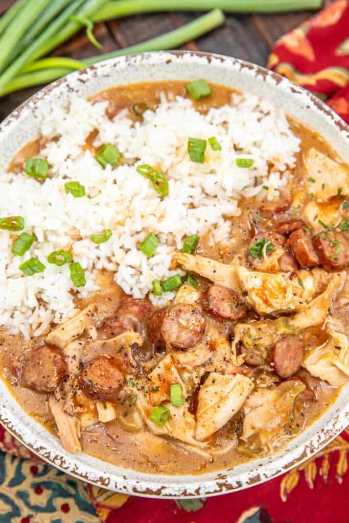 bowl of chicken & sausage gumbo topped with rice on a table