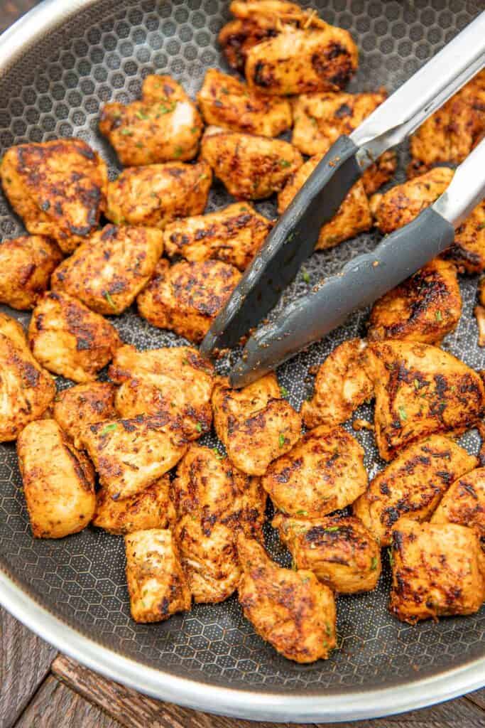 cooking chicken bites in a skillet with tongs