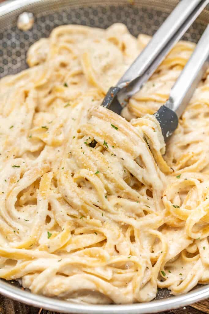 tossing fettuccine alfredo from a skillet with tongs