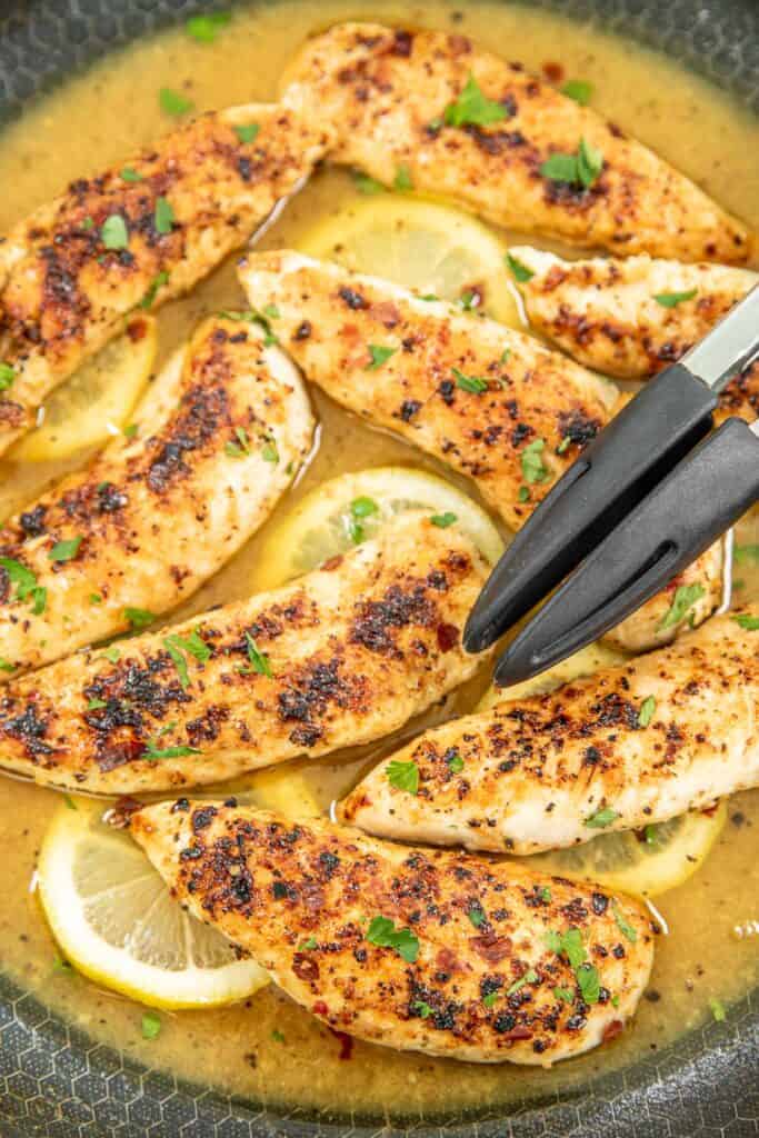 cooking chicken in lemon sauce in a skillet with tongs